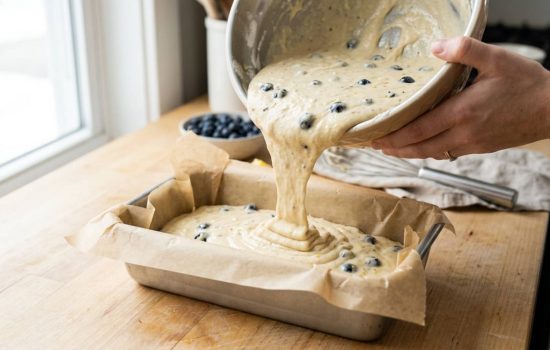 Pouring lemon blueberry batter into a prepared loaf pan.