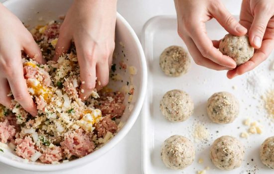 Mixing and shaping chicken meatballs by hand in a white kitchen.
