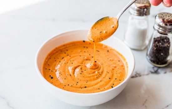 Step 4 — tasting the classic burger sauce with a small spoon in a white bowl, seasoning adjustment on white marble surface, horizontal food photography.