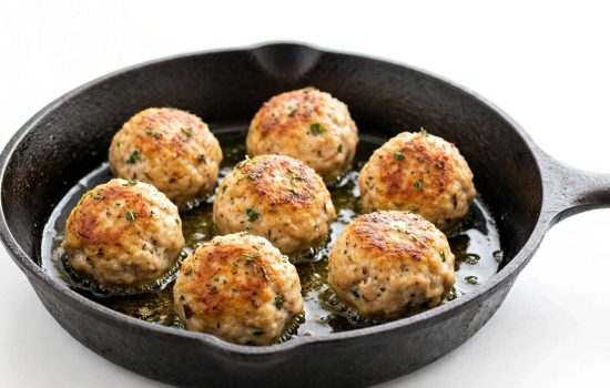 Chicken meatballs searing in a skillet until golden brown.