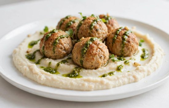 Plating chicken meatballs over pesto white bean puree with a basil pesto drizzle.