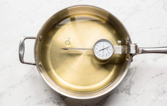 Deep frying pan filled with vegetable oil on a white countertop with a cooking thermometer showing 350°F for frying homemade churros.