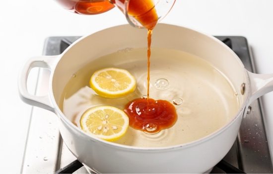 Step 2 — lemon juice being added to saucepan for seafood boil sauce base, bright clean kitchen photo