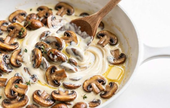 Cream and butter being stirred into browned mushrooms to make a creamy sauce.