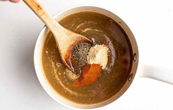 Step 3 — spices being stirred into seafood boil sauce in a white saucepan, bright clean overhead food photography