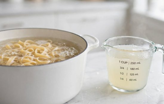 Fettuccine boiling in a pot while pasta water is reserved for the sauce.