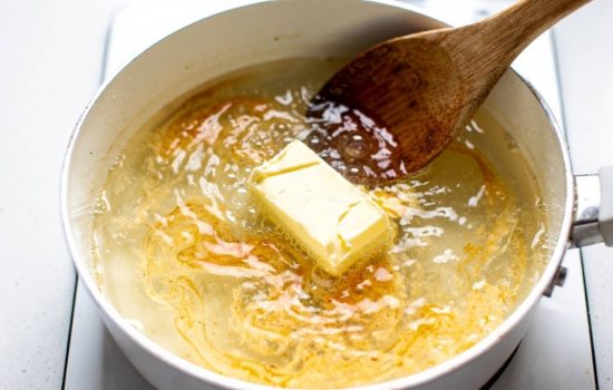 Step 4 — butter melting into simmering seafood boil sauce in a white saucepan, bright clean food photography