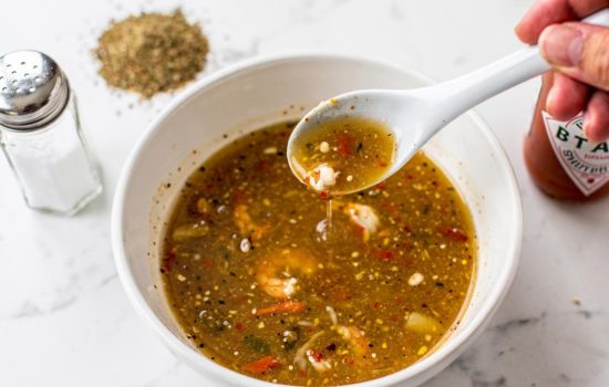 Step 5 — tasting and seasoning seafood boil sauce in a white bowl, bright overhead food photography