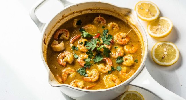 Overhead flat lay of homemade seafood boil sauce in a white bowl on a white marble table, garnished with fresh parsley and lemon wedge