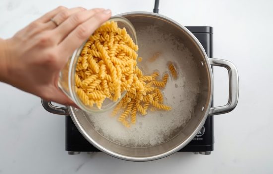 Rotini pasta being added to a large pot of boiling salted water for pasta salad