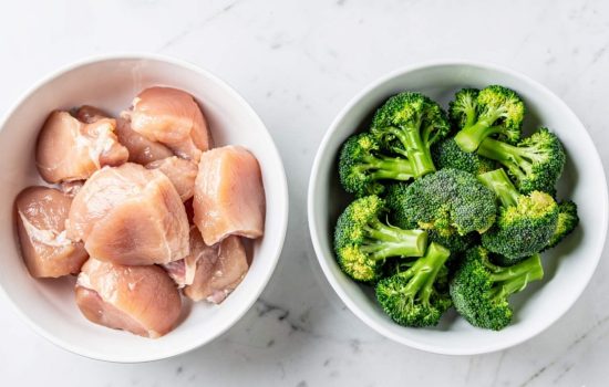 Step 1 of Easy Chicken and Broccoli Stir Fry — raw chicken being sliced on a white cutting board with broccoli florets in a bowl, bright overhead natural light, horizontal format