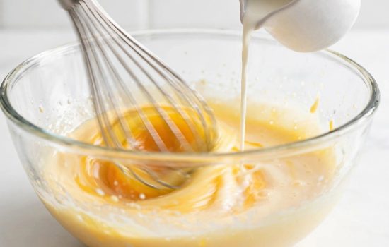 Whisking egg yolks while slowly tempering with hot milk.