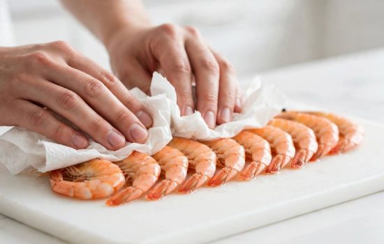 Patting cooked shrimp dry with paper towels as the first step for shrimp and avocado salad.