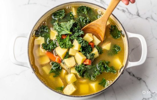 Step 4 of making Zuppa Toscana: diced potatoes and fresh spinach simmering in pot with broth, small bubbles visible on surface, steam rising, warm lighting