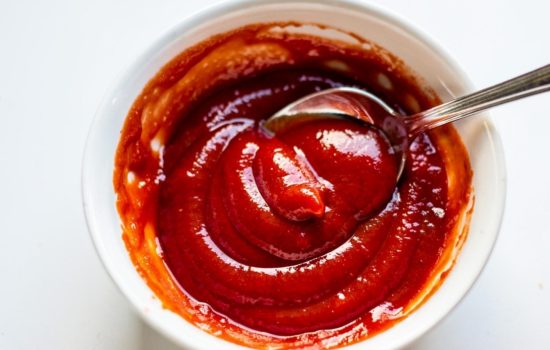 Mixing ketchup and horseradish together in a white bowl on a bright white table.