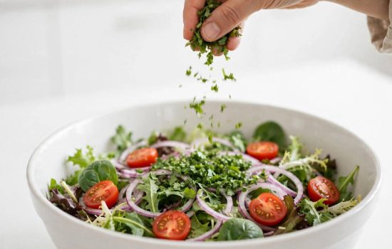 Adding greens, cherry tomatoes, red onion, and cilantro to a large salad bowl.