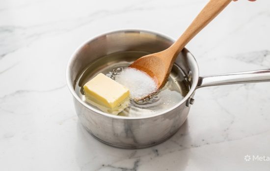 Water, butter, sugar, and salt being mixed in a saucepan on a white marble countertop to make homemade churro dough.