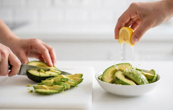 Slicing avocado and tossing it with lemon juice to prevent browning.