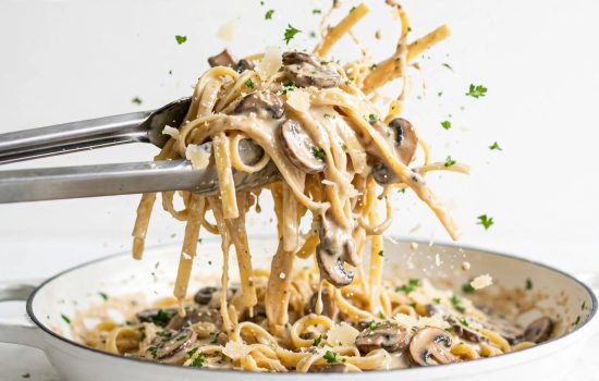 Tossing fettuccine with creamy mushroom sauce, Parmesan, and parsley in a skillet.